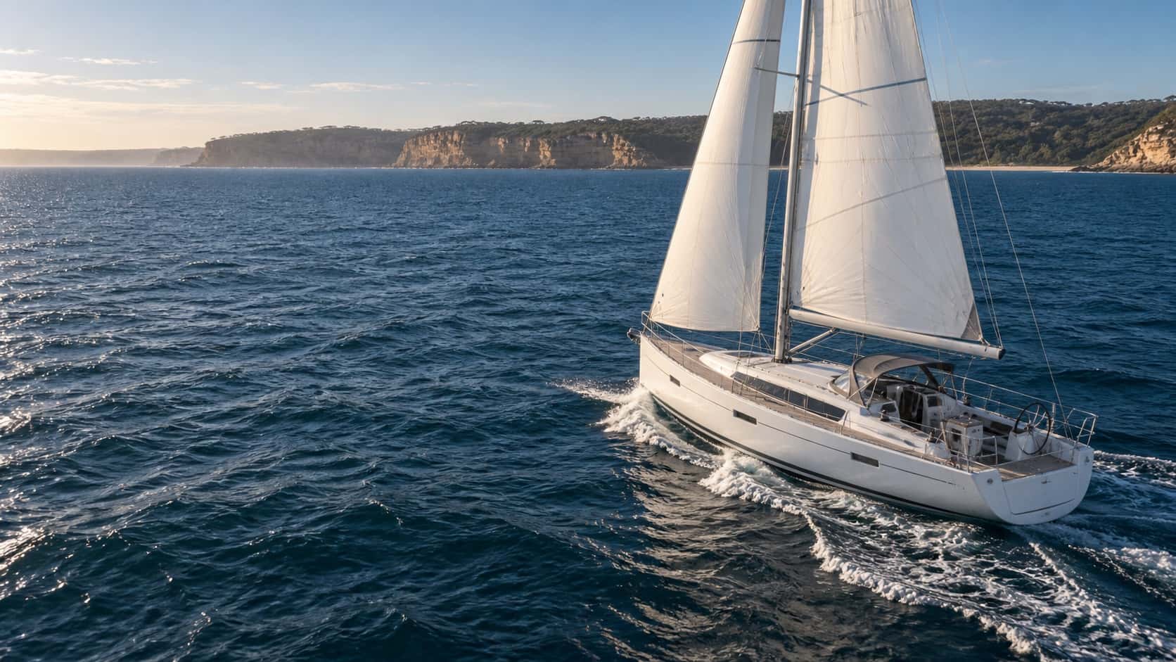 White cruising yacht sailing beside an Australian sandstone coast